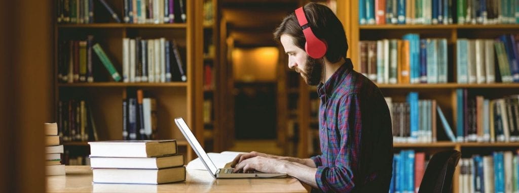 Man with headphones working on laptop in library